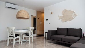 Una sala de estar moderna con un sofá gris oscuro, una mesa de comedor con sillas blancas y una lámpara colgante de fibra natural.