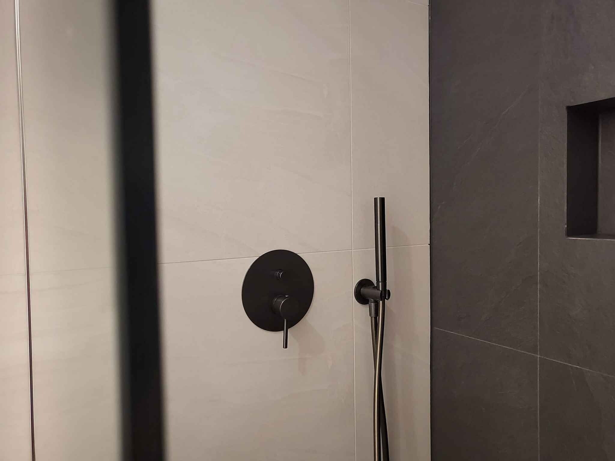 Een moderne badkamer met een minimalistisch design, voorzien van een in de muur gemonteerde douchebediening en een glazen douchecabine.