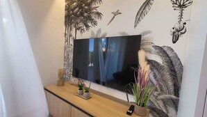Un moderno salón con un televisor de pantalla plana grande montado en la pared, con decoración de hojas tropicales y pájaros.