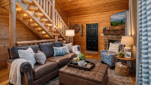 Ein Blockhaus-Interieur mit Treppe, Ledersofa, Hocker und Kamin.