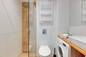 A modern bathroom with a glass shower enclosure, a white toilet, a washing machine, and a sink with a wooden countertop. - Korfu - 200 m from the Beach by Lion Apartments Sopot (Sopot)