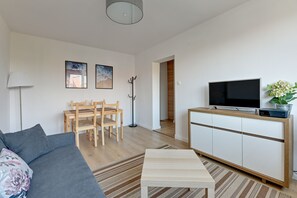 A modern living room with a sofa, a coffee table, a TV on a cabinet, a dining table with chairs, and artwork on the wall. - Korfu - 200 m from the Beach by Lion Apartments Sopot (Sopot)