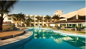 A resort with a swimming pool, palm trees, and a multi-story building with balconies. - SWISS TRAFFALGAAR LUXURY HOTELS (Nashik)