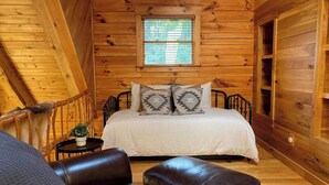 A cozy wooden cabin bedroom with a bed, two pillows, a small table with a plant, and leather chairs. - LUXE TWO | ANTLER'S GROVE *HOCKING HILLS* CLOSE TO EVERYTHING! HOT TUB, FIREPLACE,GAME ROOM,FIRE PIT (Laurelville)