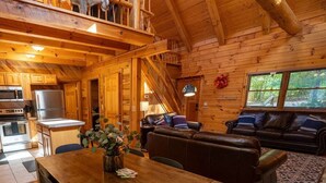 A wooden cabin interior with a dining area, kitchen, and living room. - LUXE TWO | ANTLER'S GROVE *HOCKING HILLS* CLOSE TO EVERYTHING! HOT TUB, FIREPLACE,GAME ROOM,FIRE PIT (Laurelville)