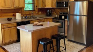 A wooden cabin-style kitchen with a central island, stainless steel appliances, and a window overlooking greenery. - LUXE TWO | ANTLER'S GROVE *HOCKING HILLS* CLOSE TO EVERYTHING! HOT TUB, FIREPLACE,GAME ROOM,FIRE PIT (Laurelville)