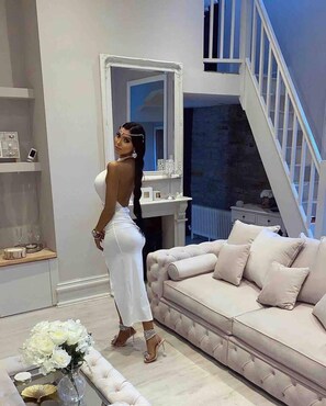 A modern living room with a large mirror, a beige sofa, and a staircase.
