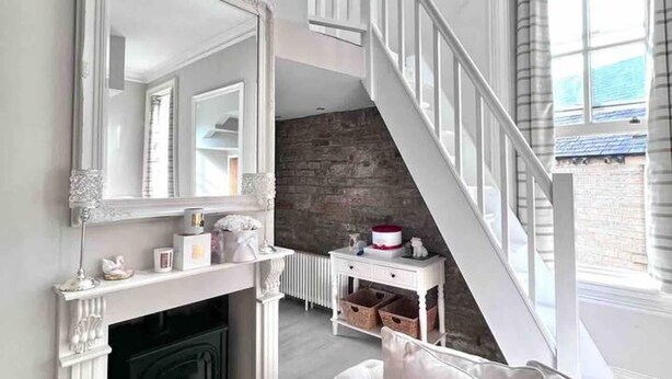 Un vaste espace de vie doté d’une cheminée, d’un grand miroir, d’un escalier et offrant une vue sur l’extérieur.