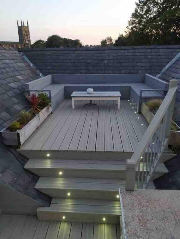 A rooftop deck with a wooden floor, a central table, and a seating area.