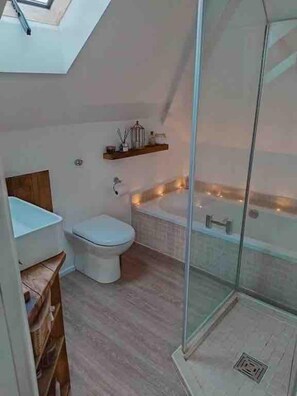 A modern bathroom with a glass-enclosed shower, a white toilet, and a wooden shelf with toiletries.