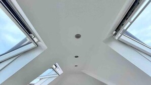 Une chambre avec un plafond en pente, un puits de lumière et un lit doté d’une tête de lit.