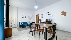 Ein modernes Wohnzimmer mit Essbereich, ausgestattet mit einem blauen Sofa, einem Holztisch und einem Fernseher.