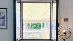 Ein Zimmer mit großem Fenster, einem Standventilator und einem gerahmten Bild an der Wand.