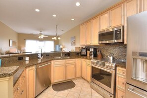 A modern kitchen with granite countertops, stainless steel appliances, and wooden cabinets. - Rock N Reel: Oceanview condo in Oak Island, sleeps up to 9 with family-friendly amenities. (Oak Island)