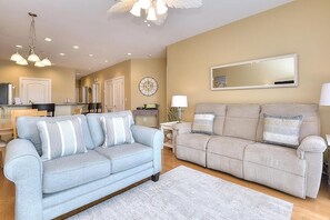 A living room with two sofas, a dining area, and a kitchen. - Rock N Reel: Oceanview condo in Oak Island, sleeps up to 9 with family-friendly amenities. (Oak Island)