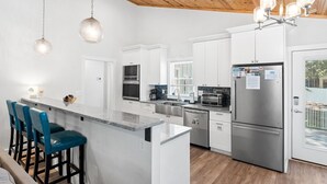 Una cocina moderna con armarios blancos, electrodomésticos de acero inoxidable y una isla central con taburetes de bar.