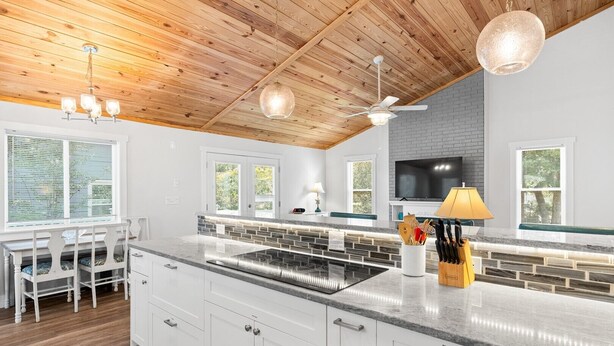 Una cocina moderna con techo de madera, armarios blancos, encimera de granito y estufa integrada.