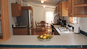 A kitchen with wooden cabinets, a stainless steel refrigerator, a stove, and a sink. There is a dining table with chairs and a bowl of fruit on the counter. - At Home Base IV, 1 of 4 units. You'll feel right at home,1/2 mile to Dreams Park (Milford)