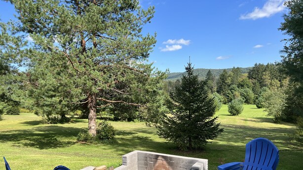 A patio area with blue Adirondack chairs, a stone fire pit, and a view of a grassy landscape with trees. - At Home Base IV, 1 of 4 units. You'll feel right at home,1/2 mile to Dreams Park (Milford)