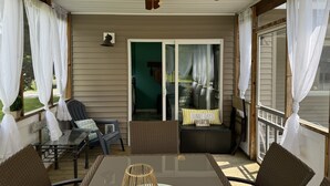 A covered patio with a ceiling fan, wicker furniture, and a glass table.