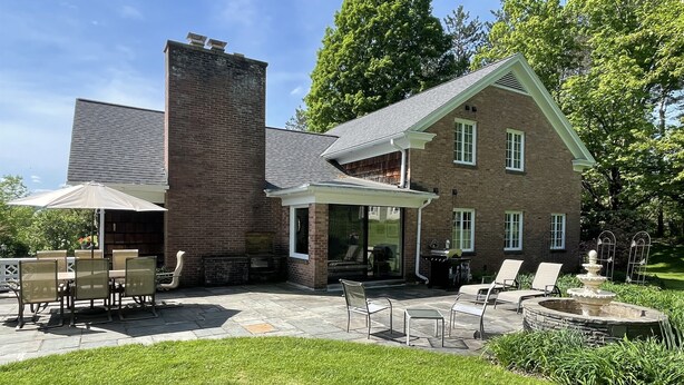 Une maison à deux étages, construite en briques, dotée d’un patio aménagé avec du mobilier d’extérieur et un foyer.