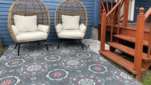Duas cadeiras de vime com almofadas, um tapete estampado e uma escada de madeira.
