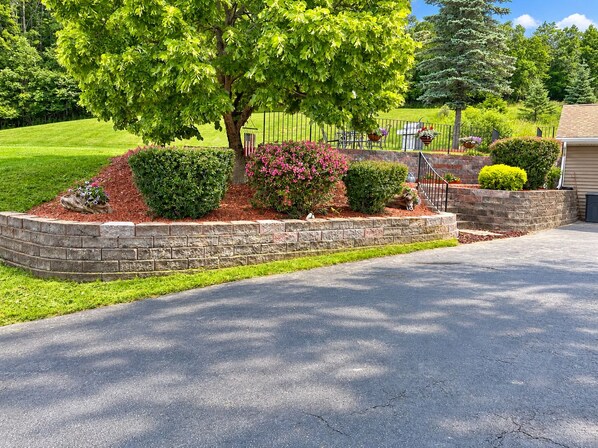 A landscaped driveway with a stone retaining wall, a tree, and a metal fence.