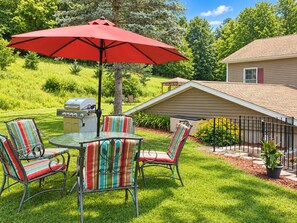 A patio with a grill, outdoor seating, and a red umbrella.