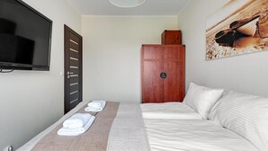 A hotel room with a bed, a TV, a wooden wardrobe, and a painting on the wall. - Lion Apartments - Parkur 2 (Sopot)