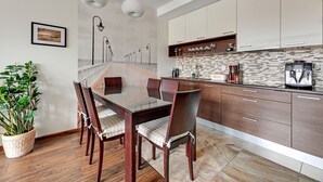 A modern kitchen with wooden cabinets, a marble countertop, and a dining area with a glass table and chairs. - Lion Apartments - Parkur 2 (Sopot)