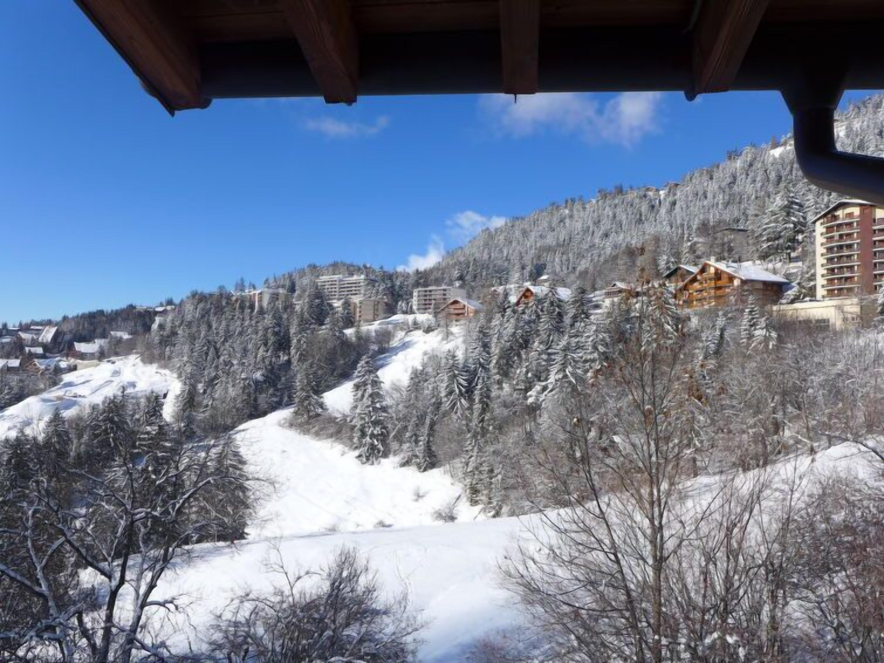Een besneeerd berglandschap met gebouwen op een helling, waaronder een groot hotel met meerdere verdiepingen en een kleinere chalet.