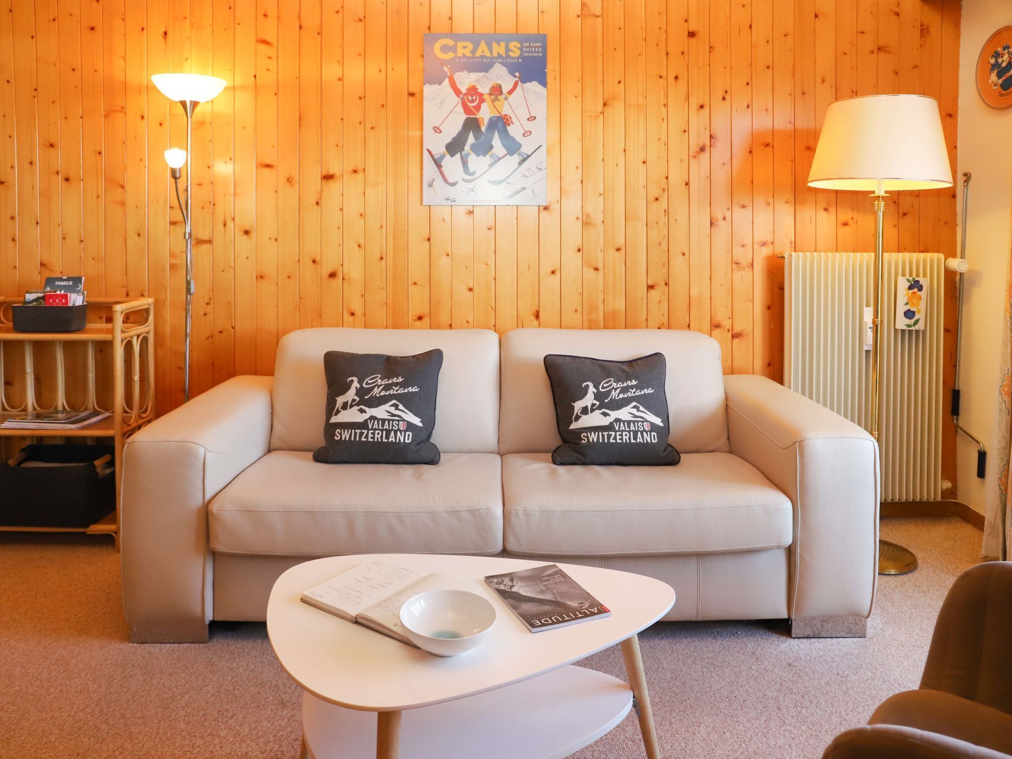 Une pièce chaleureuse avec un mur en bois, un canapé blanc agrémenté de deux coussins, une petite table sur laquelle se trouvent un bol et un livre, et une affiche accrochée au mur.