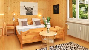 Una habitación con paneles de madera, una cama, una mesa redonda con un florero y una ventana con vistas a follaje.