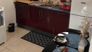 A compact kitchen with dark red cabinets, a black countertop, and a window with blinds. - 🥭Mango An Nou: A bungalow with a pool, nature, and beaches (Le Moule)