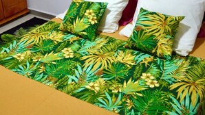 A bed with a tropical leaf pattern bedspread, a wooden headboard, and two pillows, one white and one pink. - 🥭Mango An Nou: A bungalow with a pool, nature, and beaches (Le Moule)