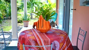 A table with a patterned tablecloth, a decorative bowl, and chairs in a covered outdoor area with a view of greenery. - 🥭Mango An Nou: A bungalow with a pool, nature, and beaches (Le Moule)