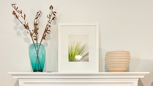 A fireplace with a white mantel, a framed picture, a vase with dried flowers, and a textured bowl. - Modern 2-bedroom 1930's Bungalow Close to Downtown (Midland)