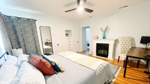 A bedroom with a bed, a dresser, a mirror, a fireplace, and a dining table. - Modern 2-bedroom 1930's Bungalow Close to Downtown (Midland)