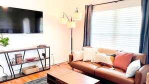 A modern living room with a leather sofa, a wooden coffee table, a TV mounted on the wall, and a floor lamp. - Modern 2-bedroom 1930's Bungalow Close to Downtown (Midland)