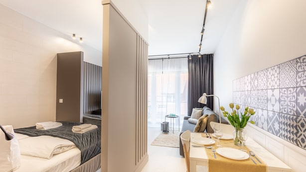 Une chambre d’hôtel moderne, équipée d’un lit, d’une table à manger dressée pour deux personnes, d’un canapé et offrant une vue sur la ville grâce à de grandes fenêtres.