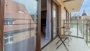 Un balcon avec une table et des chaises, une porte-fenêtre coulissante donnant sur un espace intérieur et une vue sur un bâtiment surmonté d’un dôme.