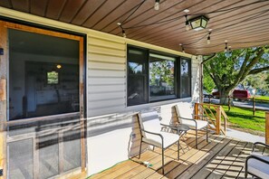 Relax on the covered patio with a wooden deck, featuring two comfortable chairs and a sheltered space with large windows.