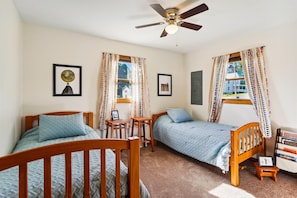 A room with two wooden beds, a ceiling fan, and a window with patterned curtains.