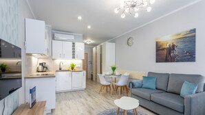 Una cucina moderna con mobili bianchi, una zona pranzo con un divano grigio e sedie bianche, e un quadro raffigurante una spiaggia al muro.