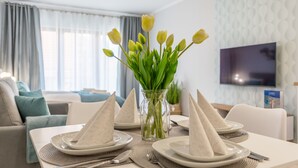 Zona pranzo con tavolo apparecchiato per quattro persone, un vaso con tulipani gialli e una TV a schermo piatto montata a parete.