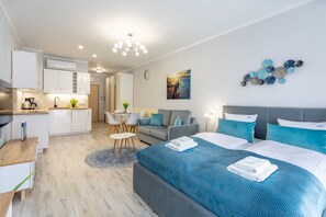 A modern hotel room with a large bed, a sofa, a dining area, and a kitchenette.