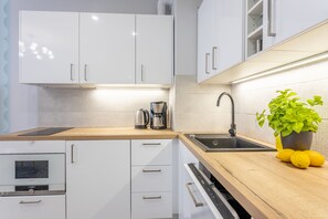 A modern kitchen with white cabinets, a wooden countertop, a built-in oven, a sink, and a potted plant with lemons.