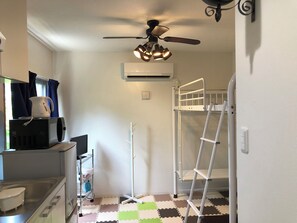 Cucina compatta con microonde, bollitore e lavandino. Si vedono un ventilatore a soffitto e un condizionatore d'aria. Un letto a castello è posizionato contro il muro.