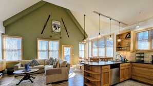 A spacious living room with a high ceiling, a kitchen with wooden cabinets, and a dining area. - Stunning/Walk to Summer Festivals/Hot Tubs (Keystone)