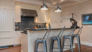 Et køkken med hvide skabe, en mørk backsplash og en central ø med barstole.